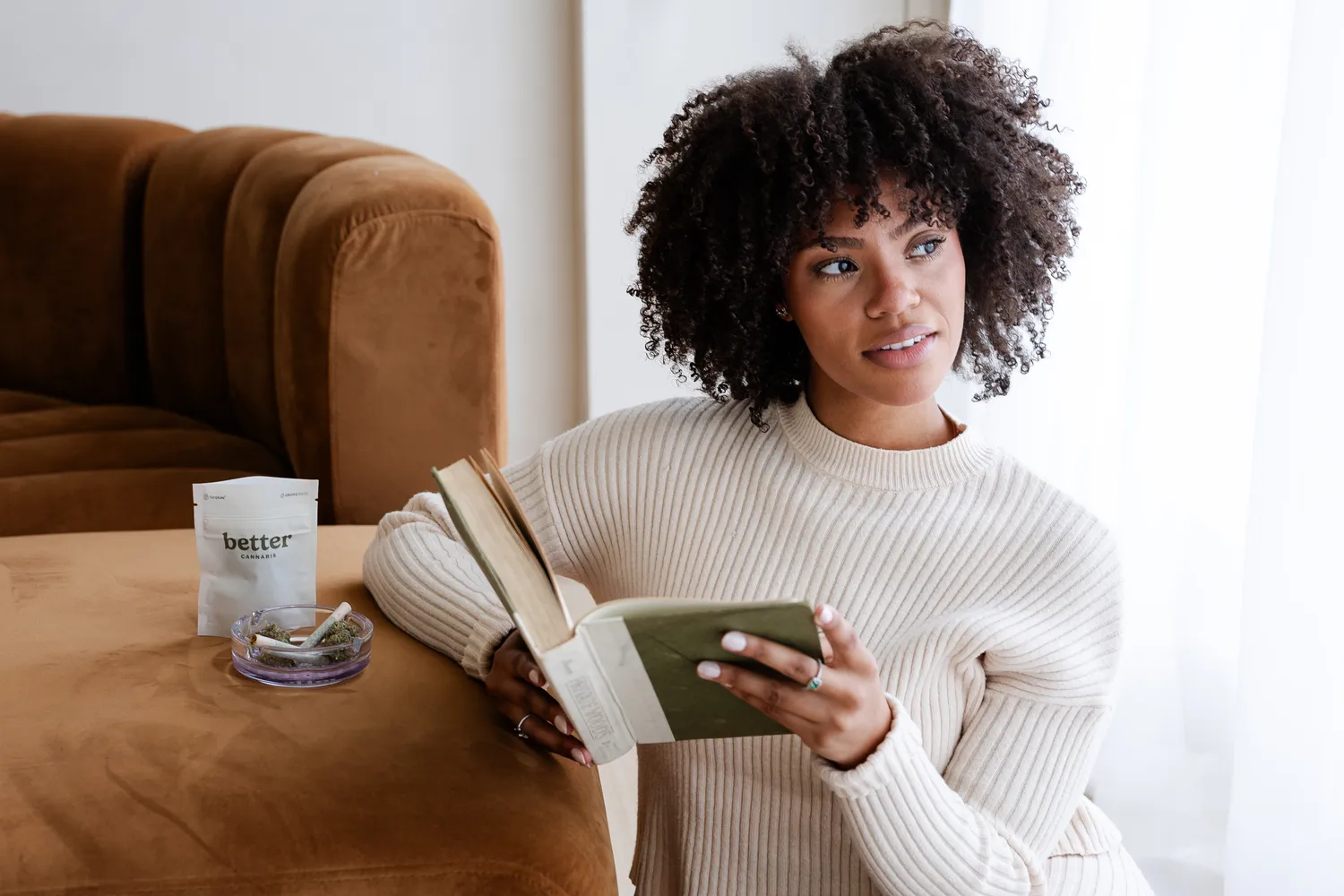 A Better Cannabis customer relaxing at home, reading on a couch with a Better product nearby